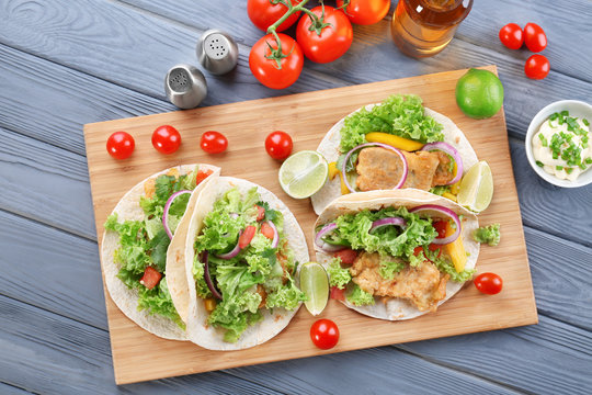 Wooden board with delicious tacos on kitchen table