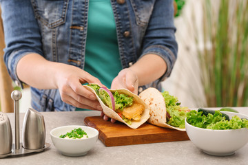 Woman holding delicious fish taco in kitchen