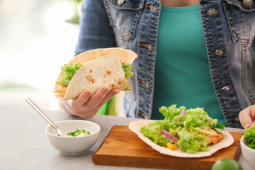 Woman holding delicious fish taco in kitchen