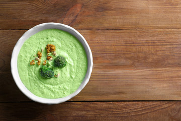 Delicious creamy broccoli soup with walnut in bowl on wooden background