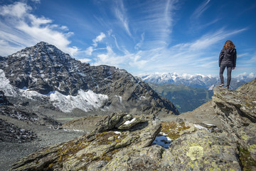 Naklejka na ściany i meble une jeune femme brune debout et de dos admire un paysage de montagne avec des cimes enneigées