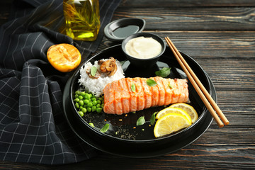 Plate with slice of delicious salmon, rice and fish sauce on table