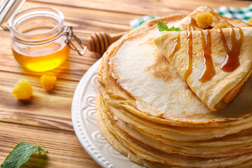 Stack of thin pancakes served with yellow raspberry and honey