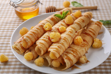 Rolled thin pancakes served with yellow raspberry and honey on white plate