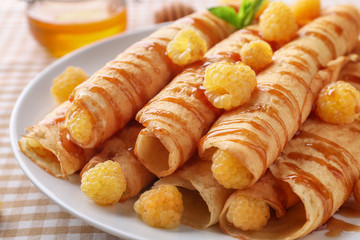 Rolled thin pancakes served with yellow raspberry on white plate