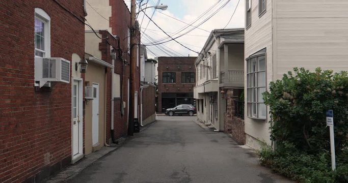 A daytime establishing shot of an empty alleyway in a small town in America.  	