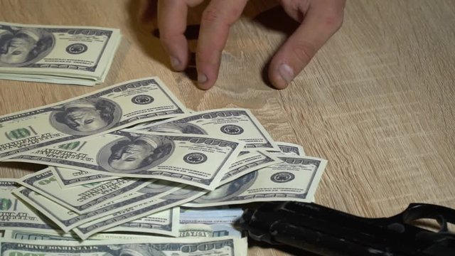 The collector taps a finger on the table near the gun while on the table I throw one hundred dollar bills