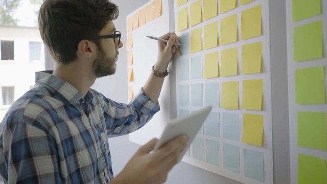 Young focused man planning with tablet and sticky notes