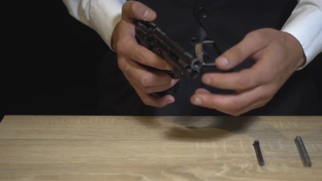Gangster in a suit compiles on the table a gun