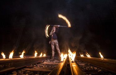 Woman spinning fire staff while standing on railroad tracks at night