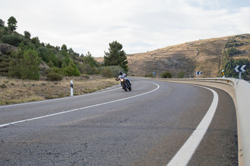 Fototapeta premium Young man riding a motorcycle on road turning in a curve in the mountains on sunny day. 