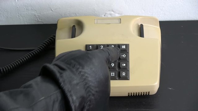 Gangster hand with black leather glove pressing numbers buttons on classic retro old phone telephone 
