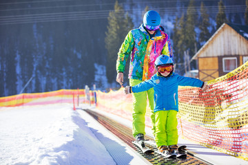 Young boy and his father standing on travelator in children's area on skiing resort