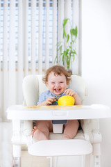 Cute baby boy eating by himself on high chair