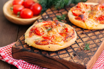 Mini pizzas margheritas on served on a wooden board. Wooden background