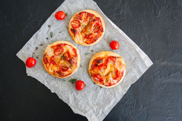 Mini pizzas margheritas on a parchment paper on a black stone background