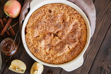 Traditional American apple pie in a ceramic form and ingredients on a wooden table. Close up and overhead view.