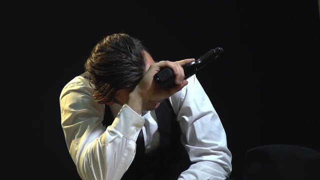 Tired man in a suit sits at the table with pistols to his hand and straightens his hair