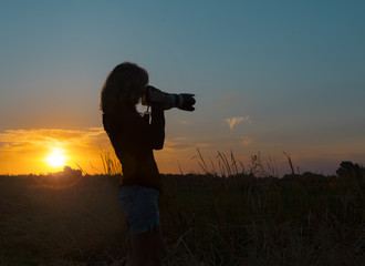 Fototapeta premium Sunrise silhouette of woman photographer at work