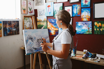 Portrait of young beautiful middle age white Caucasian woman artist drawing painting in art studio with acrylic paints on canvas. View from back. Lifestyle activity hobby concept
