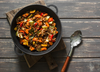 Lentils and seasonal garden vegetables braised in the pan on wooden background, top view. Autumn vegetarian healthy lunch