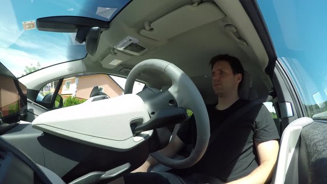 CLOSE UP, LOW ANGLE VIEW: Man driving in innovative autonomous automated electric car using self-parking autopilot for parallel parking on street. Robotic computer turning wheel in autosteering mode