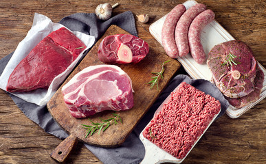 Different types of raw meat on a rustic wooden background.