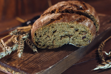 a piece of bread on a wooden  board close up among wheat ears.