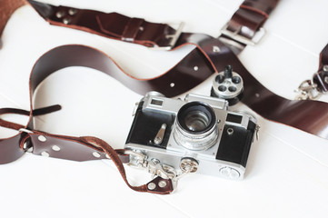Vintage camera with brown leather strap on a white wooden background