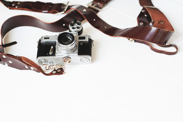 Vintage camera with brown leather strap on a white wooden background. space for text