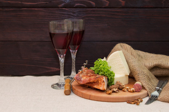 Meat, cheese and wine glasses on a table with linen cloth on background of wooden planks