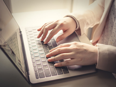 close up left hand of business woman(30s to 40s) with pink or pastel suits working with her computer laptop with soft focus right hand and background