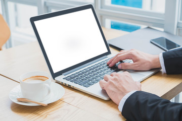 Hand of Businessman typing on laptop with smartphone and coffee cup in home office or co working space.Concept of workplace using mobile technology.