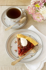 Piece of plum galett with cream and tea. Dessert. Rustic style, selective focus.