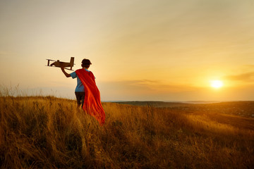 A boy in the costume of  pilot walking on the field at sunset.