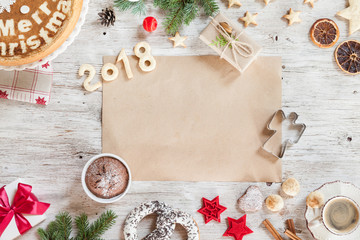 Homemade Christmass cookies, number year 2018, desserts, gift, cinamon, berries, dried orange, hazelnuts, cup of coffee, red christmas tree toys on a beige wooden background.