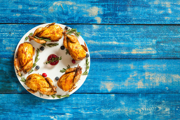 Baked quails on white plate. Christmas dish on a blue wooden table. Top view. Copy space. Winter holidays concept. Culinary background for recipe of christmas dishes.