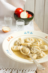 Pelmeni with broth on a wooden table with a snack and vodka.