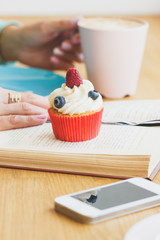 Cup with cappuccino, cupcake and a book with a phone
