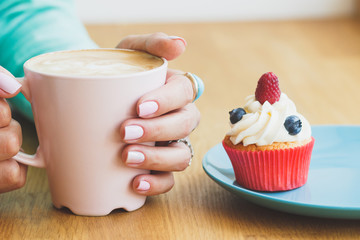 Woman's hands with a cup of coffee and a cupcake on the plate