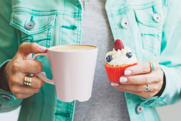 Woman's hands with a cup of coffee and a cupcake