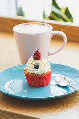 Cupcake with raspberry and blueberry on the plate, cup of hot cappuccino