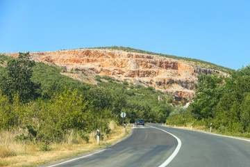 Car on a road through the rural landscape with quarry under clear blue sky.