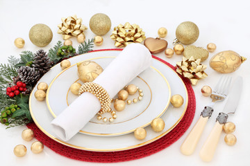 Christmas dinner table setting with porcelain plates, napkin, gold bauble decorations, cutlery,...