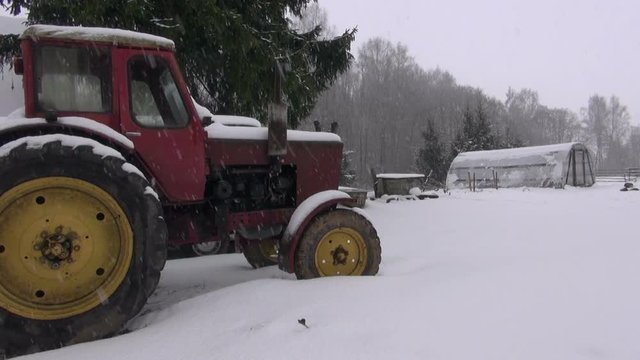 Snowfall in farm on old retro tractor and plastic greenhouse