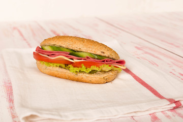 Sandwich with cheese, tomato, salami, cucumber and lettuce on wooden table