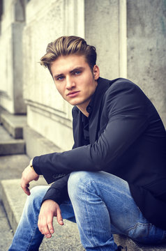 Handsome blond young man sitting on stone stair steps outside of big door