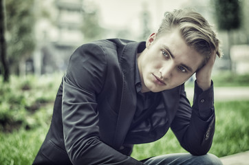 Close up Disappointed Young White Man Sitting at Street Side with Grassy Landscape at the Background