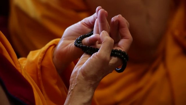 Buddhist monk praying - hands and beads rosary closeup