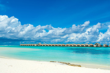 Beautiful tropical landscape. Wooden villas over water of the Indian Ocean. Sandy beach with sunbeds and umbrellas.